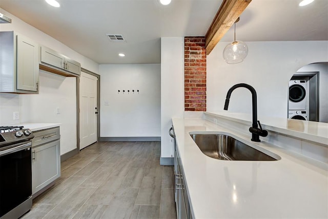 kitchen with sink, pendant lighting, electric stove, stacked washer and clothes dryer, and light wood-type flooring