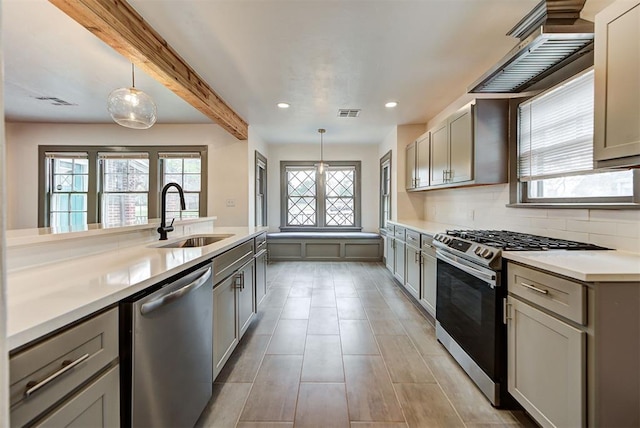 kitchen with stainless steel appliances, light countertops, a sink, and hanging light fixtures