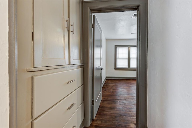 hallway featuring visible vents, baseboards, and dark wood-type flooring