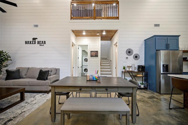 dining space featuring stacked washer / dryer, wooden walls, ceiling fan, and concrete floors