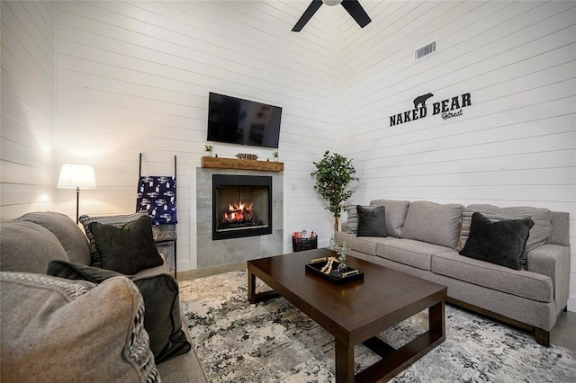 living room featuring ceiling fan, a fireplace, a high ceiling, and wooden walls