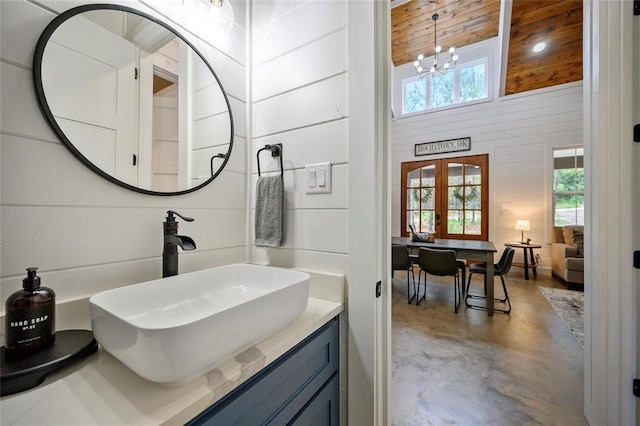 bathroom featuring french doors, an inviting chandelier, a towering ceiling, concrete flooring, and vanity