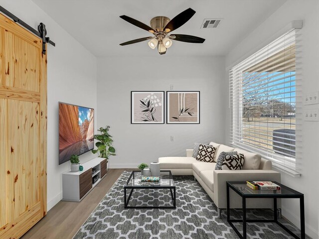 living room with a barn door, ceiling fan, and wood-type flooring