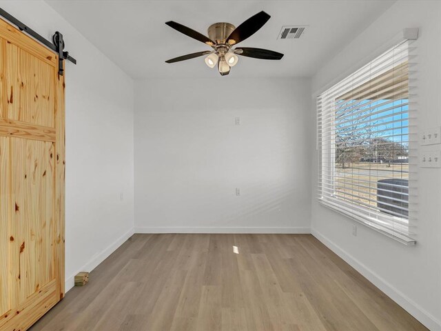 empty room with light wood-type flooring, a barn door, and ceiling fan