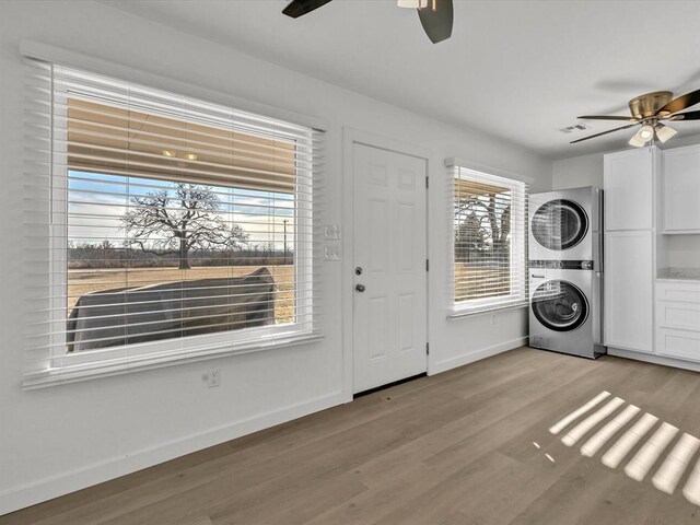 clothes washing area with ceiling fan, stacked washing maching and dryer, and light wood-type flooring