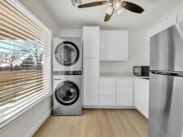 laundry area with light hardwood / wood-style floors, ceiling fan, and stacked washer and clothes dryer