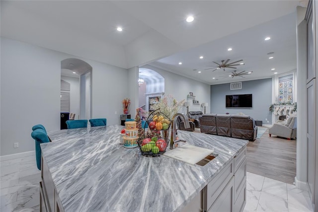 kitchen featuring ceiling fan, sink, a kitchen island, light stone counters, and white cabinets