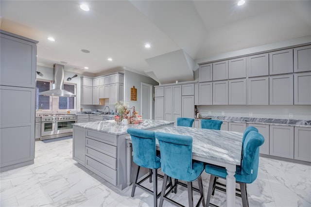 kitchen with a kitchen breakfast bar, light stone counters, island range hood, double oven range, and gray cabinets