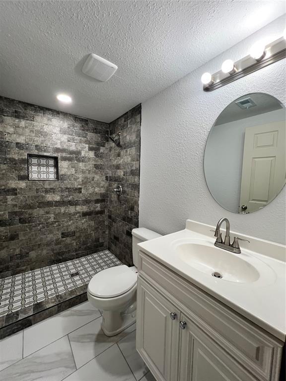 bathroom featuring vanity, toilet, a textured ceiling, and a tile shower