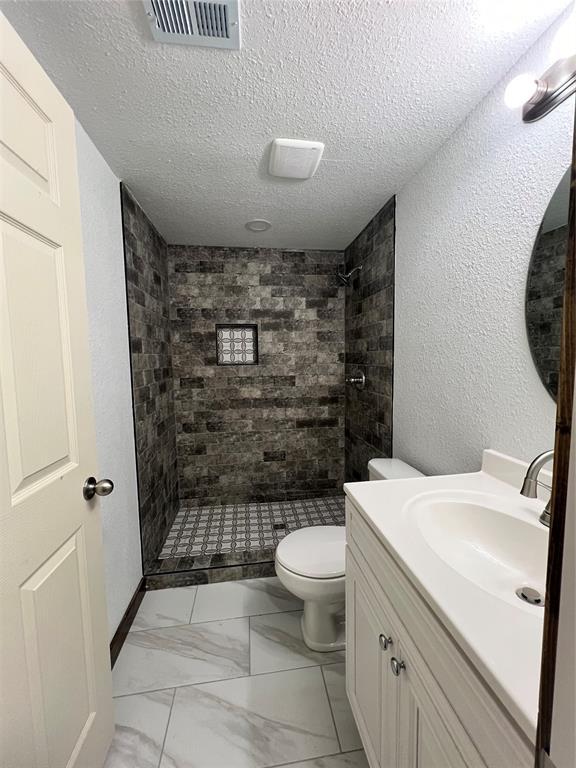 bathroom with a tile shower, vanity, a textured ceiling, and toilet