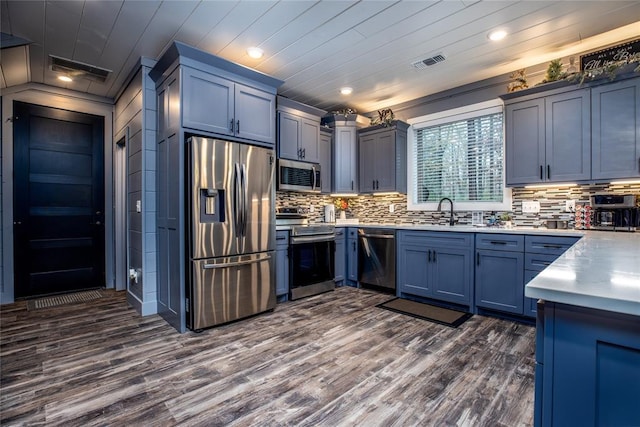 kitchen featuring ornamental molding, stainless steel appliances, dark wood-type flooring, sink, and blue cabinetry