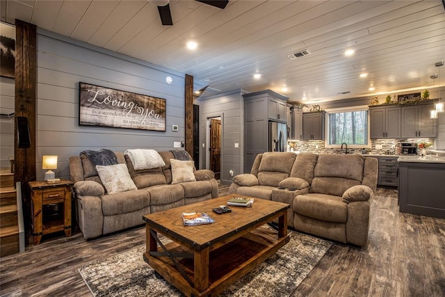 living room with dark hardwood / wood-style flooring, wooden ceiling, wooden walls, and sink
