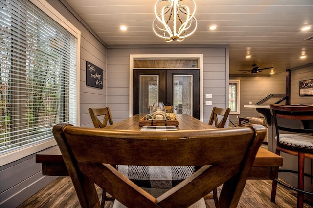 dining area with hardwood / wood-style floors, ceiling fan with notable chandelier, wooden walls, and french doors