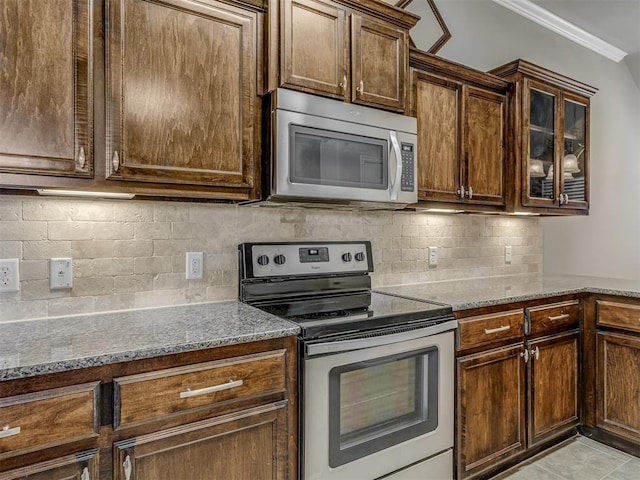 kitchen with stone counters, ornamental molding, appliances with stainless steel finishes, tasteful backsplash, and light tile patterned flooring