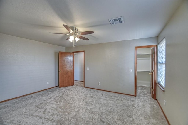 unfurnished bedroom featuring ceiling fan, a walk in closet, light carpet, and a closet