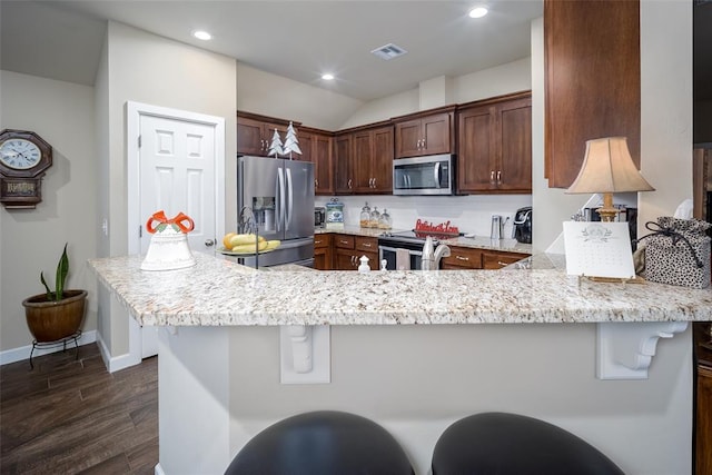 kitchen featuring backsplash, light stone countertops, appliances with stainless steel finishes, kitchen peninsula, and a breakfast bar area