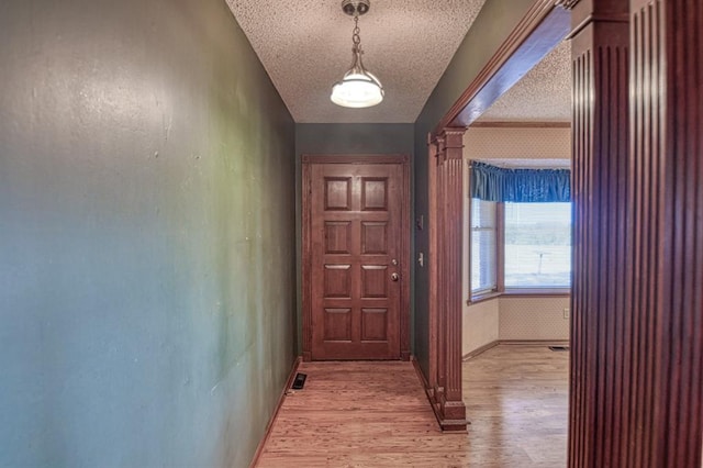 doorway to outside with decorative columns, light hardwood / wood-style flooring, and a textured ceiling