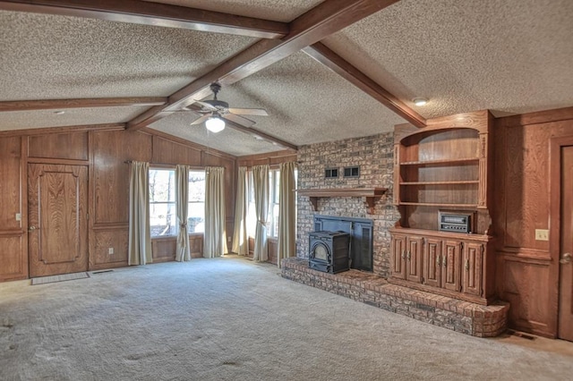 unfurnished living room featuring carpet flooring, a wood stove, wooden walls, and a textured ceiling