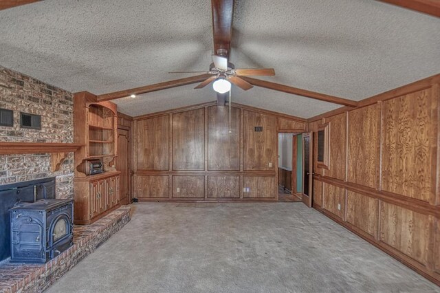 unfurnished living room with a wood stove, wood walls, light carpet, and a textured ceiling