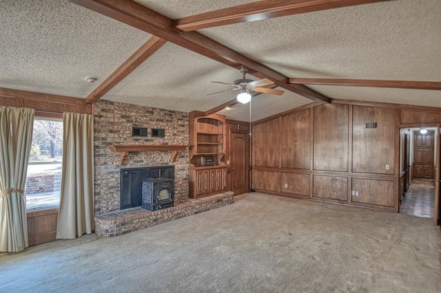 unfurnished living room with a textured ceiling, a wood stove, light carpet, and wooden walls