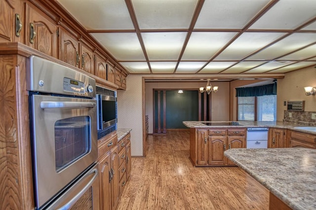 kitchen featuring stainless steel microwave, an inviting chandelier, sink, light hardwood / wood-style floors, and kitchen peninsula