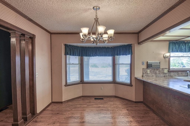 unfurnished dining area featuring sink, a notable chandelier, wood-type flooring, a textured ceiling, and ornamental molding