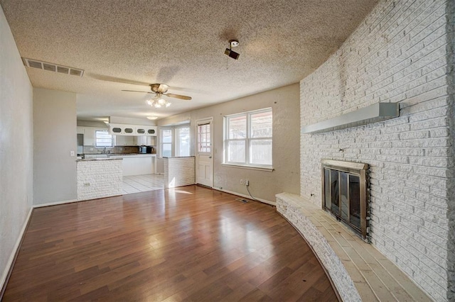 unfurnished living room with ceiling fan, wood-type flooring, a textured ceiling, and a brick fireplace