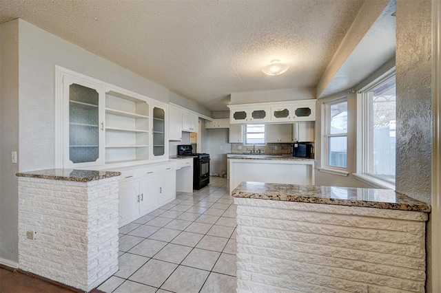 kitchen with light tile patterned flooring, kitchen peninsula, black range with gas cooktop, a textured ceiling, and white cabinets