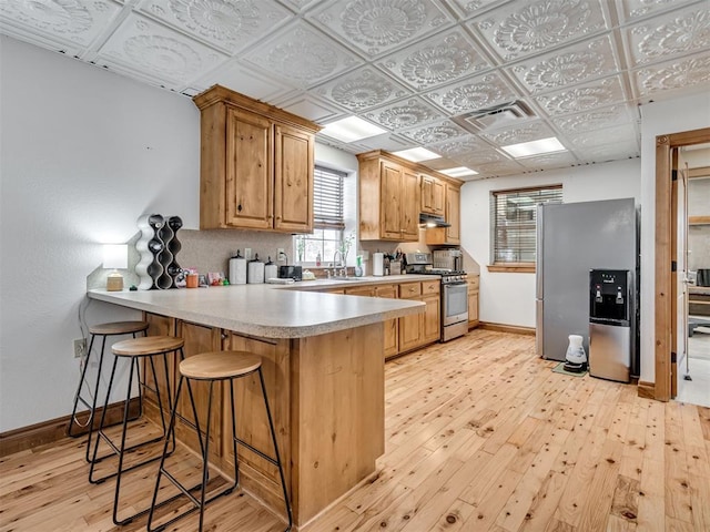 kitchen with a breakfast bar, sink, light hardwood / wood-style flooring, kitchen peninsula, and stainless steel appliances