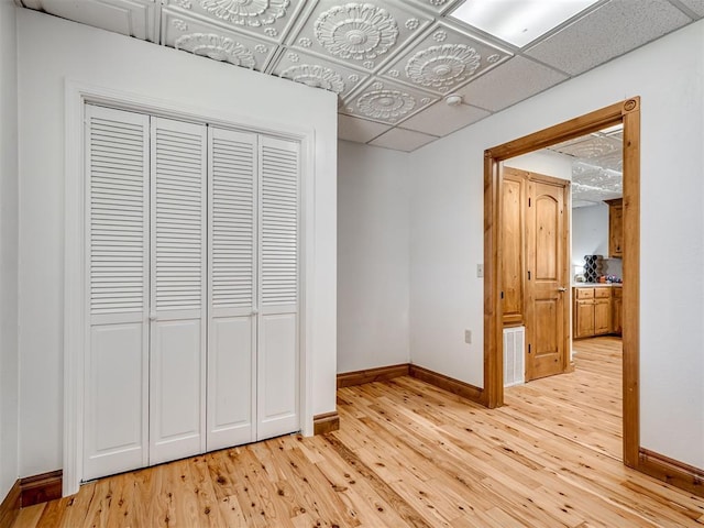 unfurnished bedroom with a drop ceiling, light wood-type flooring, and a closet