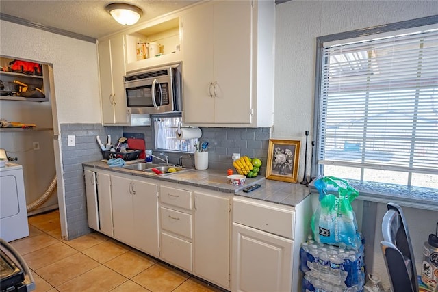 kitchen featuring backsplash, sink, light tile patterned floors, washer / clothes dryer, and white cabinetry