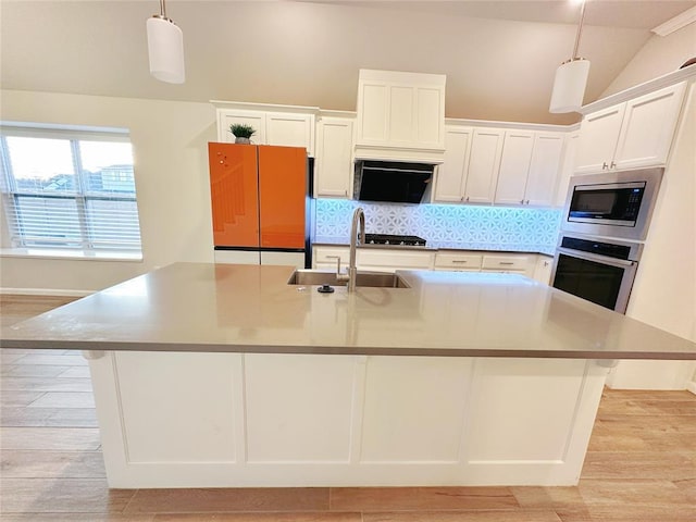 kitchen with stainless steel appliances, a kitchen island with sink, sink, pendant lighting, and white cabinets