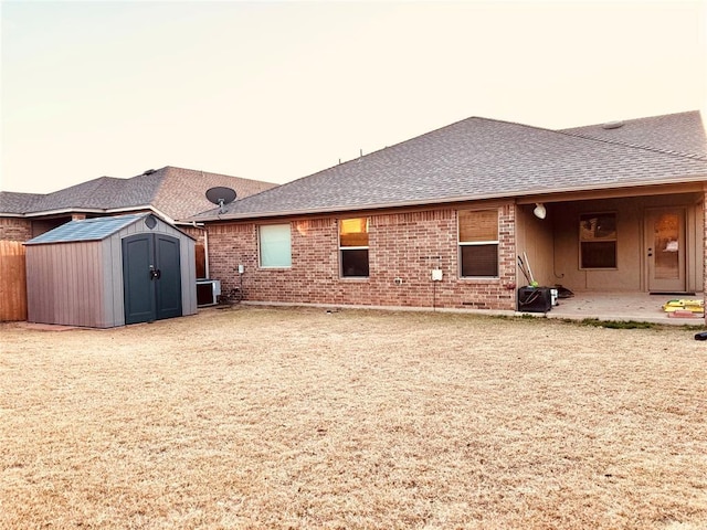 back of property with brick siding, roof with shingles, a storage shed, an outbuilding, and a patio