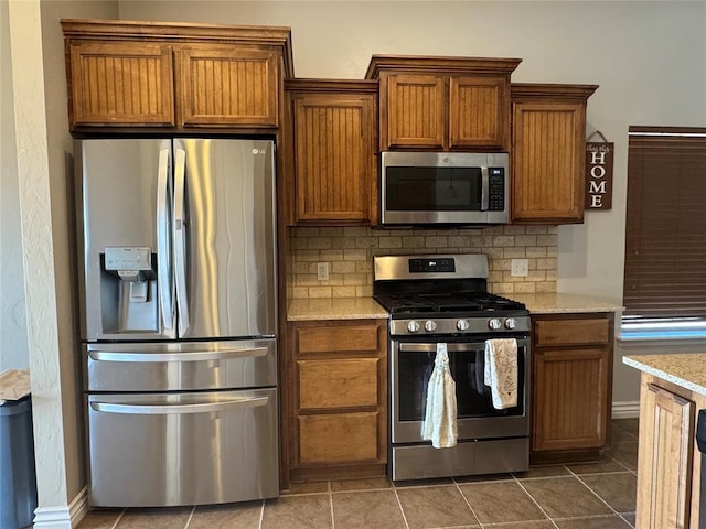 kitchen featuring tile patterned floors, tasteful backsplash, appliances with stainless steel finishes, and brown cabinetry