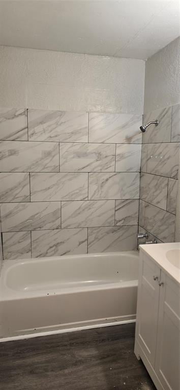 bathroom with hardwood / wood-style flooring, vanity, and tiled shower / bath