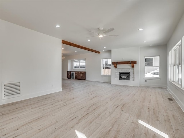 unfurnished living room featuring a tile fireplace, ceiling fan, plenty of natural light, and light wood-type flooring