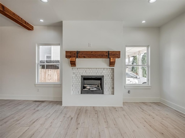 unfurnished living room with a fireplace, light hardwood / wood-style flooring, and beamed ceiling