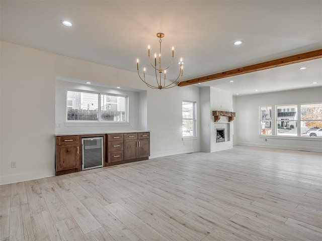 unfurnished living room with beam ceiling, wine cooler, light hardwood / wood-style flooring, and a notable chandelier