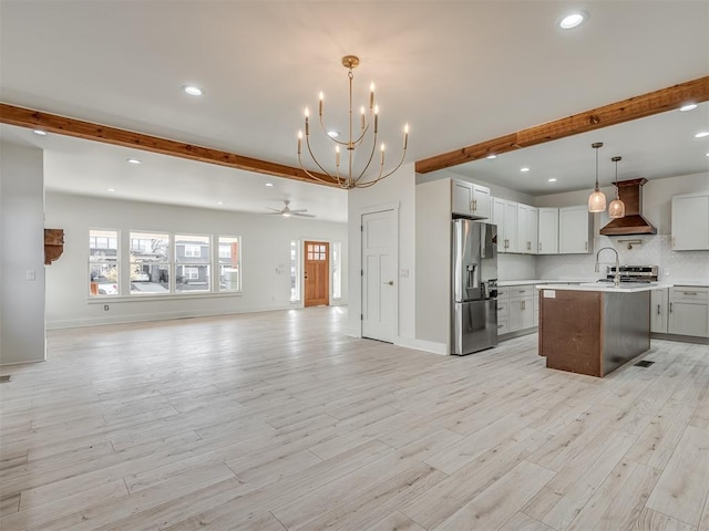 kitchen with appliances with stainless steel finishes, light wood-type flooring, hanging light fixtures, and a kitchen island with sink