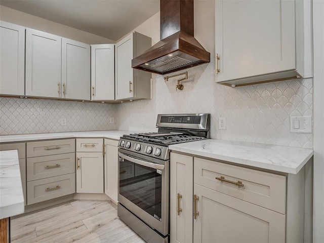 kitchen featuring light stone countertops, wall chimney range hood, tasteful backsplash, stainless steel range with gas cooktop, and light wood-type flooring