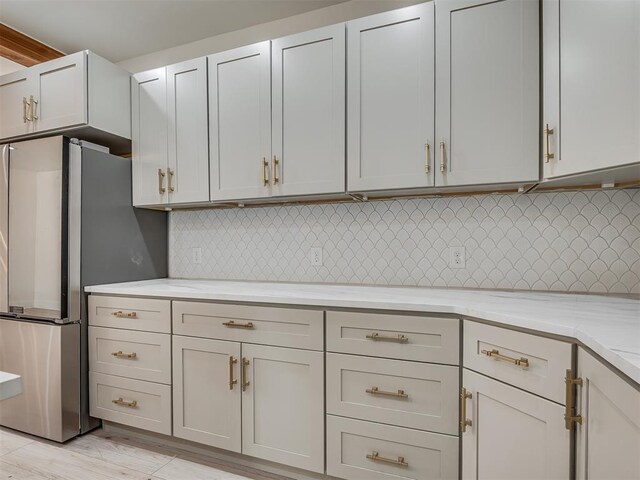 kitchen with decorative backsplash, stainless steel fridge, light stone counters, and light wood-type flooring