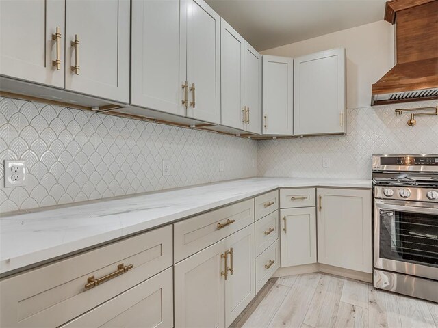 kitchen with light stone countertops, light hardwood / wood-style flooring, stainless steel range oven, decorative backsplash, and custom range hood