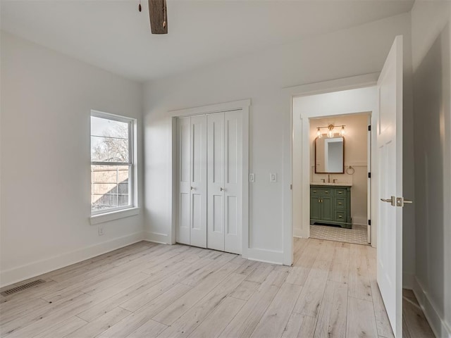 unfurnished bedroom with ceiling fan, light wood-type flooring, ensuite bathroom, and a closet