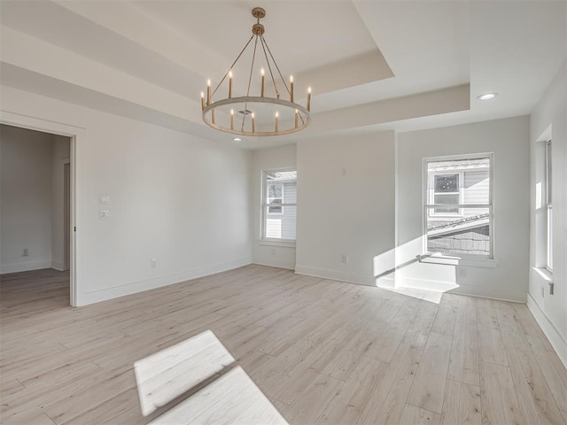 unfurnished room with an inviting chandelier, light hardwood / wood-style flooring, a wealth of natural light, and a tray ceiling