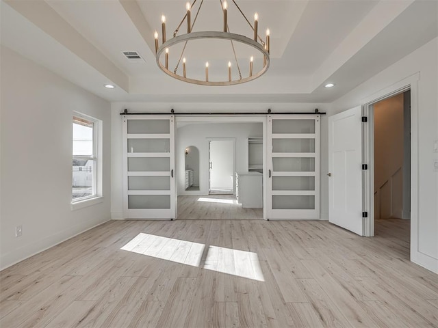 unfurnished living room featuring a raised ceiling, a barn door, and light hardwood / wood-style floors