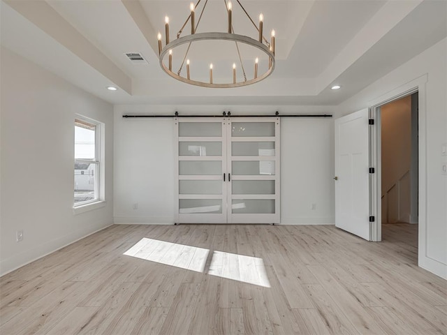 interior space featuring a chandelier, a barn door, light hardwood / wood-style floors, and a tray ceiling