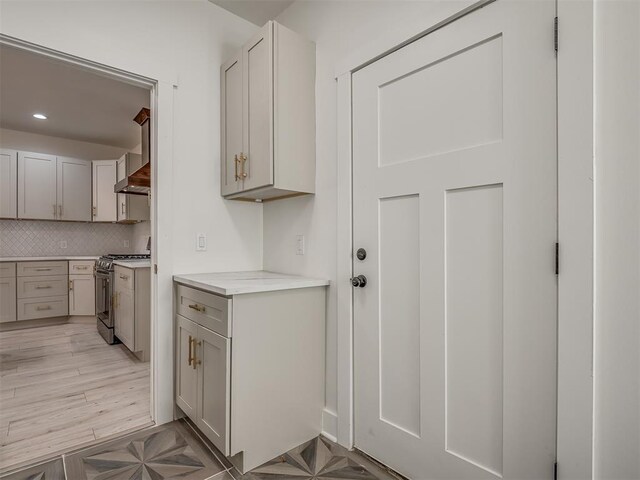 kitchen with tasteful backsplash, light hardwood / wood-style flooring, wall chimney range hood, and stainless steel range with gas stovetop