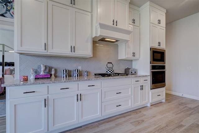 kitchen with appliances with stainless steel finishes, light wood-type flooring, light stone counters, custom exhaust hood, and white cabinetry