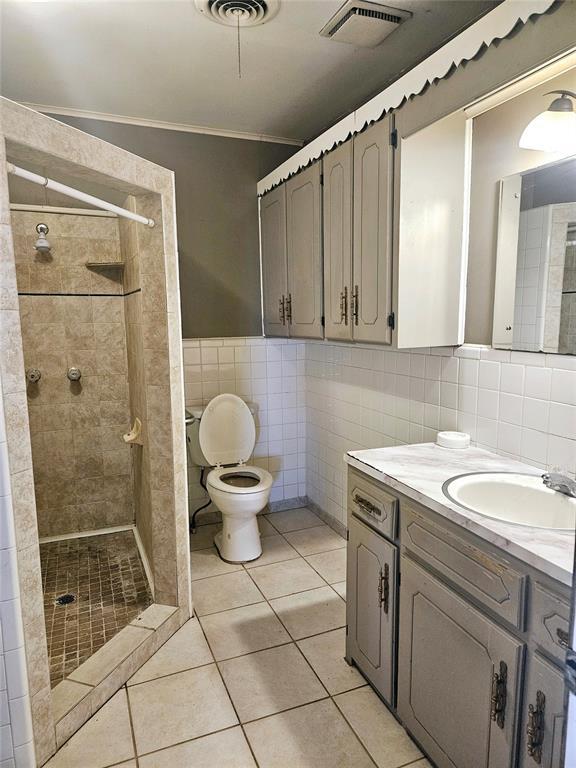 bathroom featuring tile patterned flooring, vanity, tiled shower, and tile walls