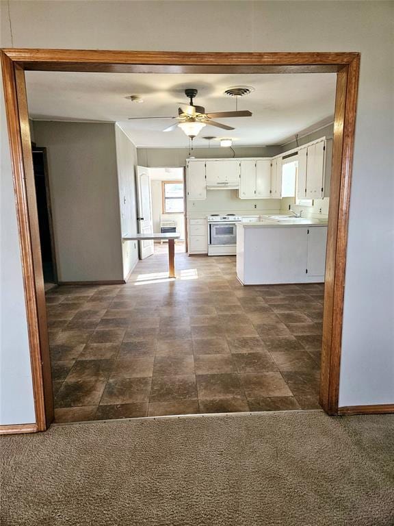 kitchen featuring white electric range oven, ceiling fan, a healthy amount of sunlight, dark colored carpet, and white cabinets